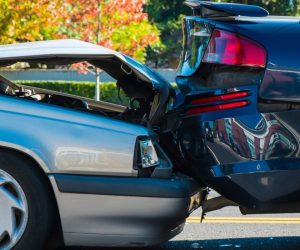 A silver car rear-ended a dark blue car on the road, causing visible damage to both vehicles’ bumpers.